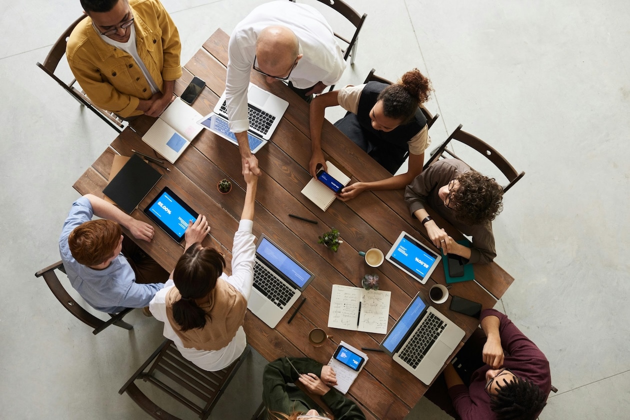 Team collaborating around a wooden table with laptops and digital devices during a meeting.