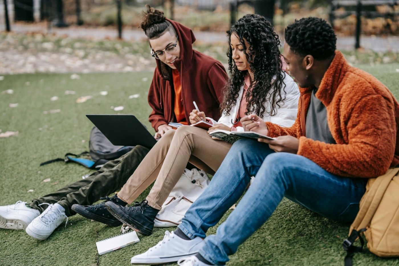 Three students studying together on campus sitting on the grass.