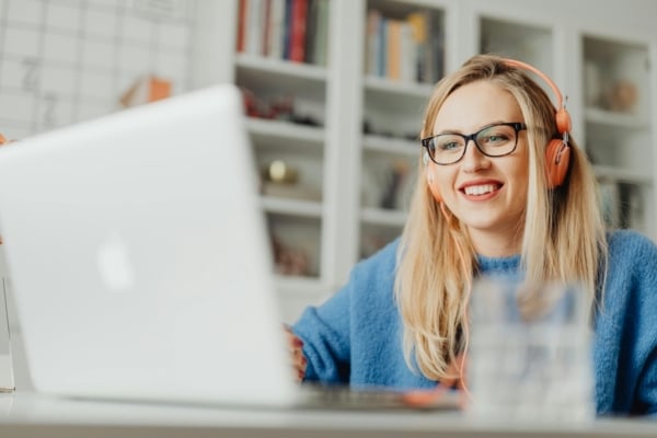 Young woman smiling during an online class while wearing headphones and using a laptop