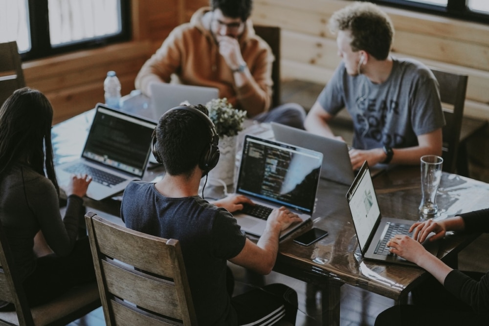 Team of developers collaborating with laptops around a table in a workspace