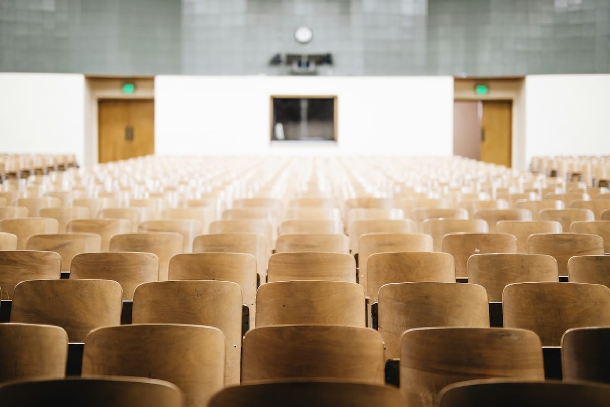 An empty university lecture hall with rows of wooden seats facing the front.