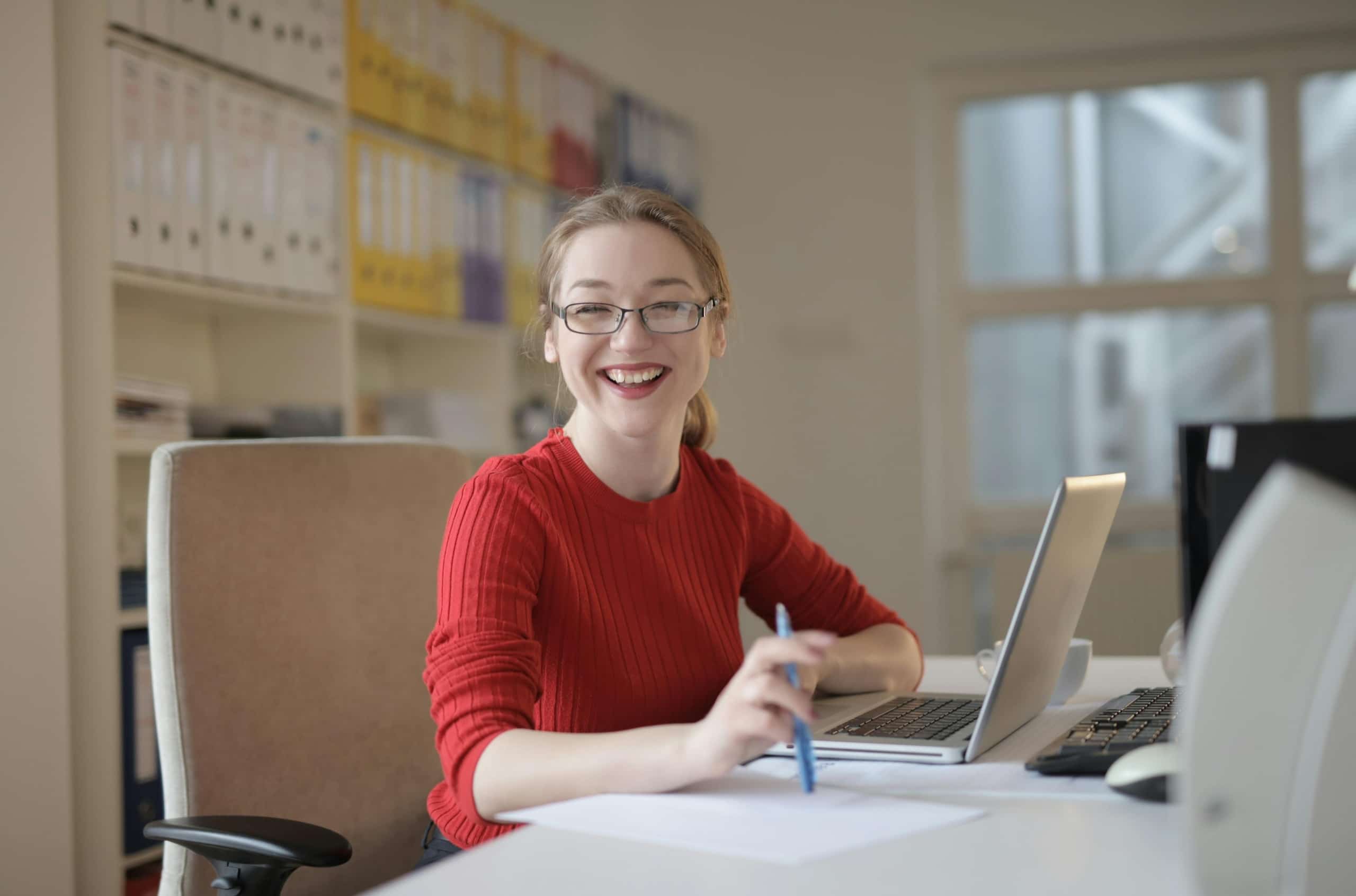 A happy college donor sits at a desk with her laptop.