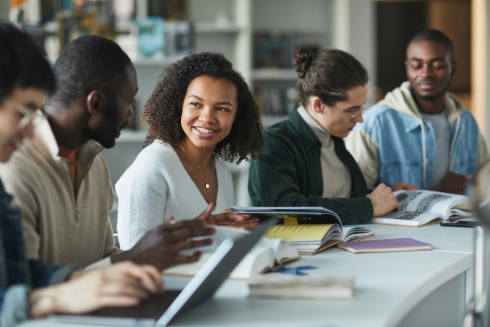 Group of diverse students studying and chatting around a table in a library