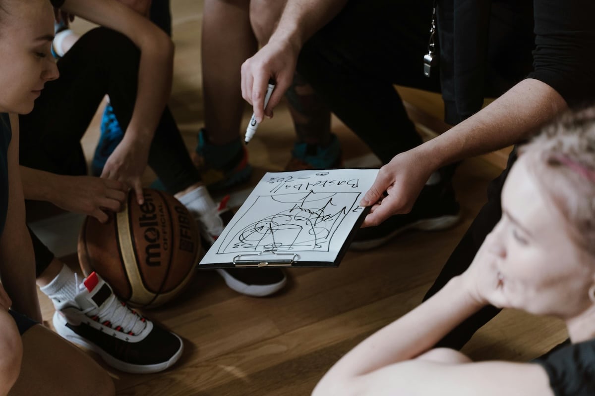 Basketball coach using whiteboard to explain play strategy to players in a gym setting