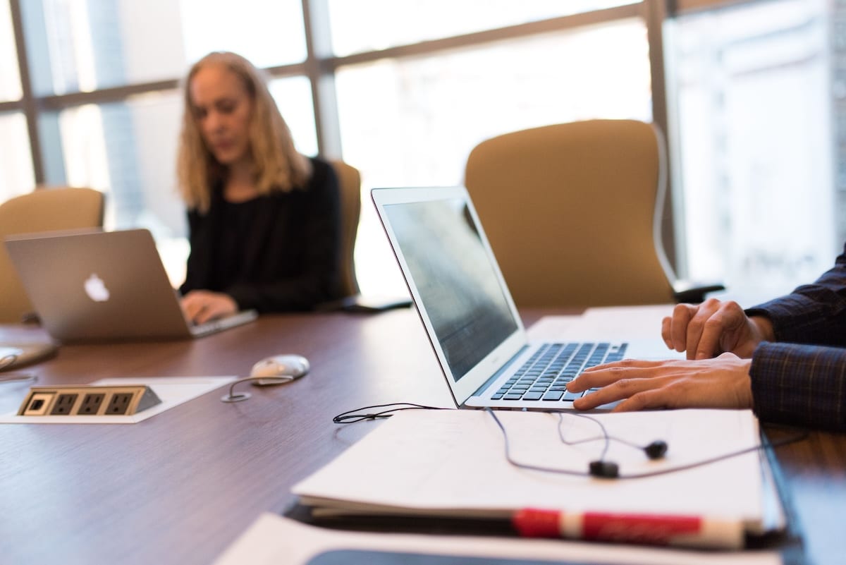 Two colleagues working on laptops at a conference table in a bright meeting room