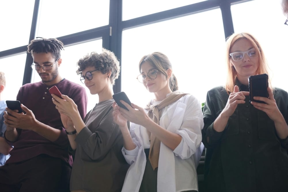 Young diverse group of people using smartphones in front of large windows