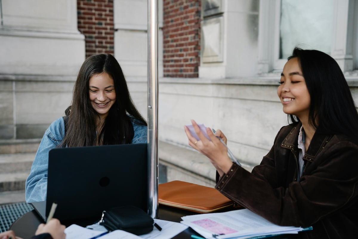 Two female students studying together at an outdoor table on campus