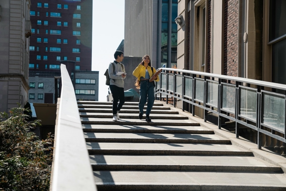 Two students walking down a staircase outside a university building on a sunny day.