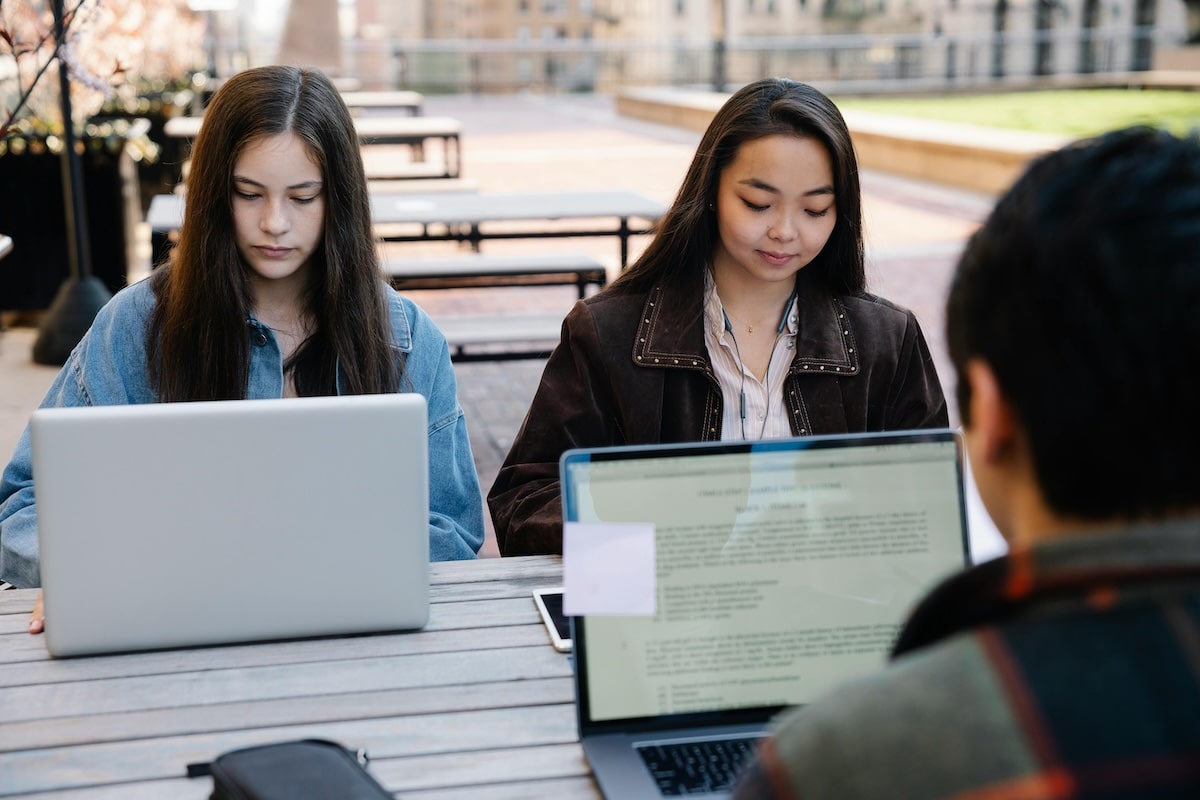 College students working on laptops together at an outdoor campus table
