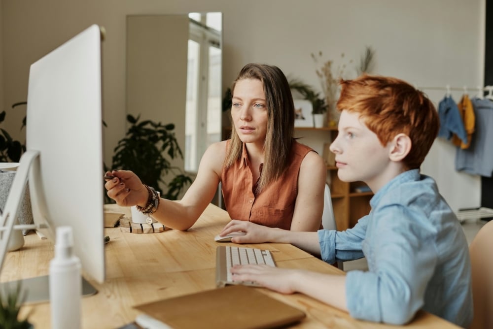 Woman helping a child use a desktop computer in a home setting