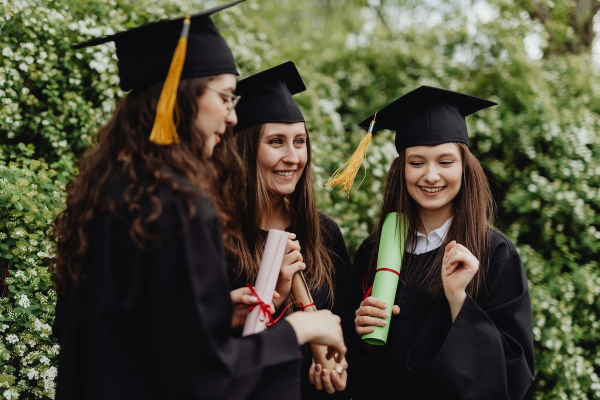 Three happy female graduates in caps and gowns celebrating with diplomas in hand