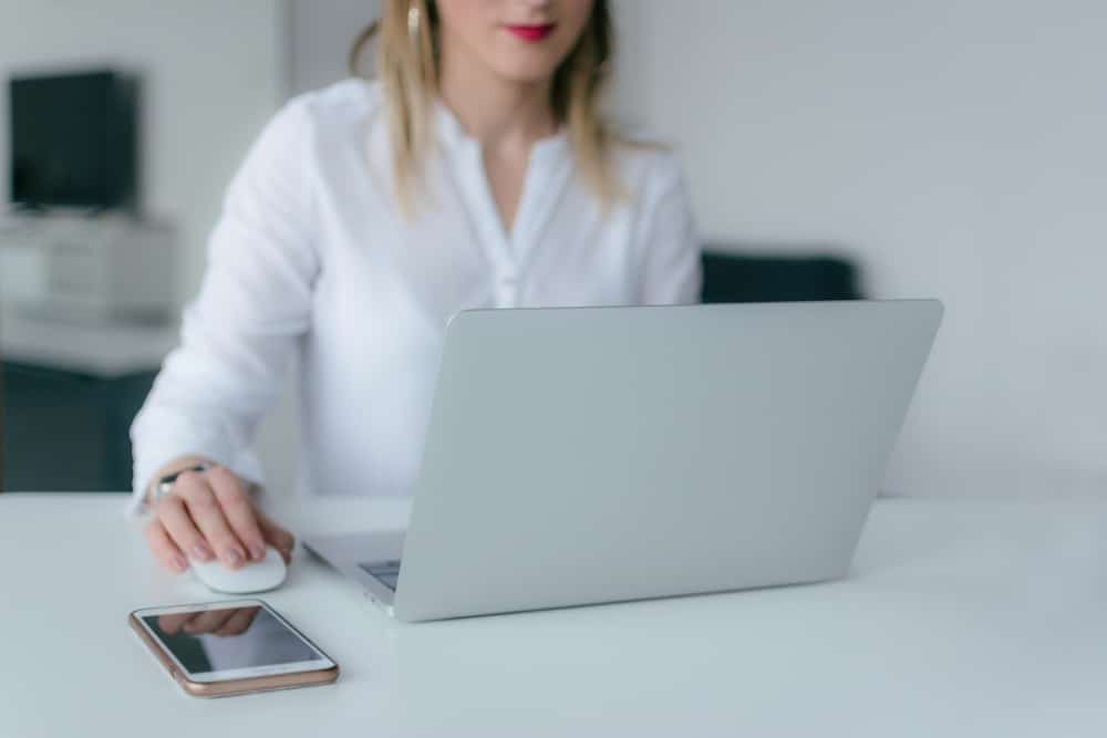 Focused Remote Work from Minimalist Office Woman in white blouse working on laptop with smartphone nearby.