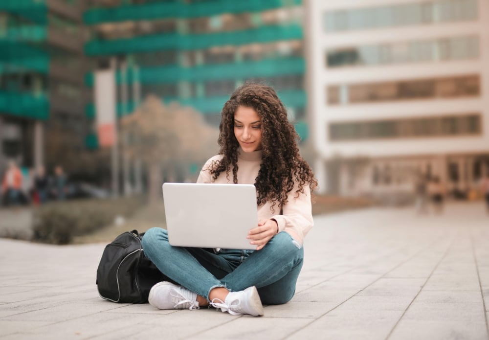 A student sits on the ground with her laptop.