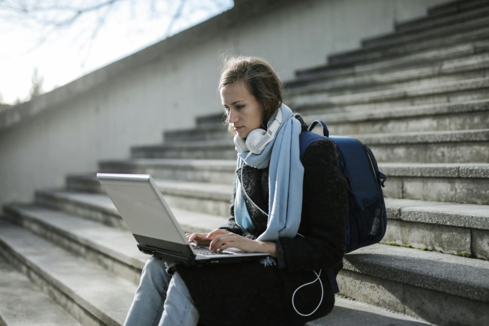 A woman sitting on concrete stairs using a laptop.