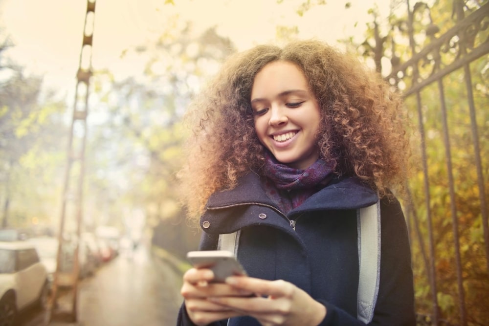 Smiling young woman using smartphone on a city sidewalk in autumn