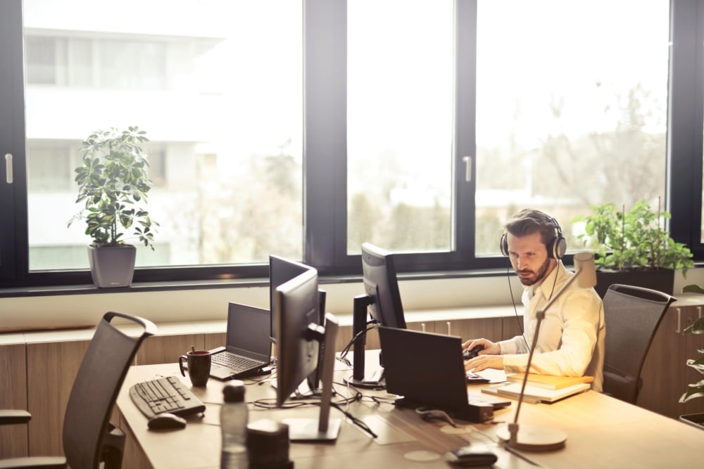 Focused man with headset working at multi-monitor office desk.