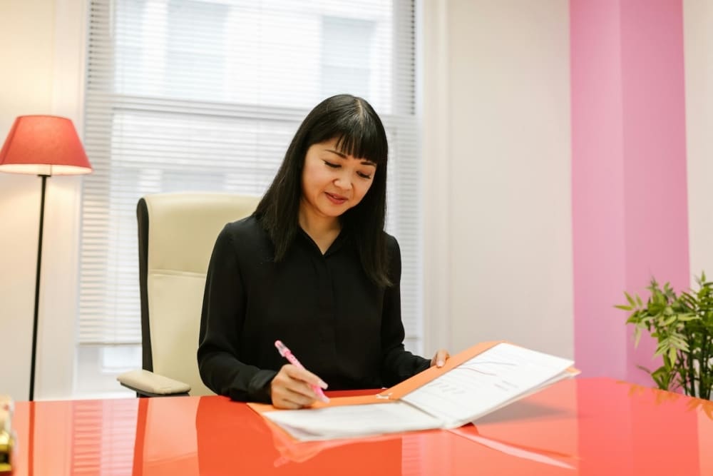 A higher education administrator reviews student outreach documents at her desk, focused and working through the details.