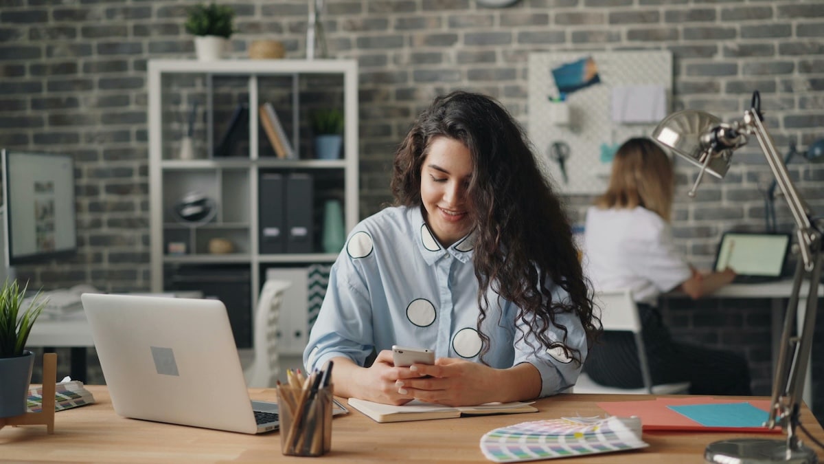 Young professional smiling while using smartphone at a desk in a modern office
