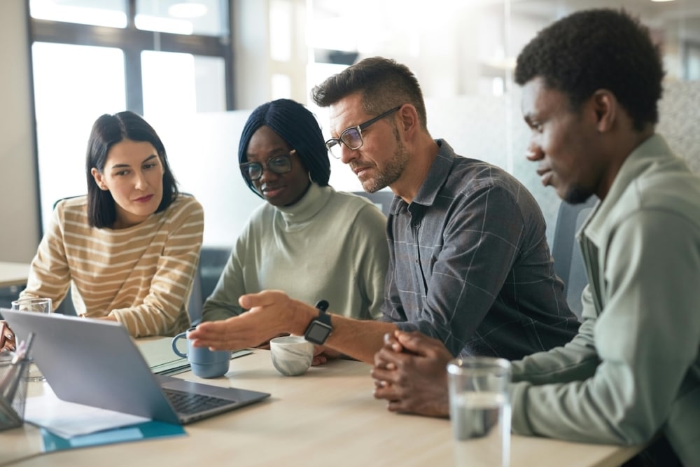Team of diverse professionals collaborating at a modern office table with a laptop