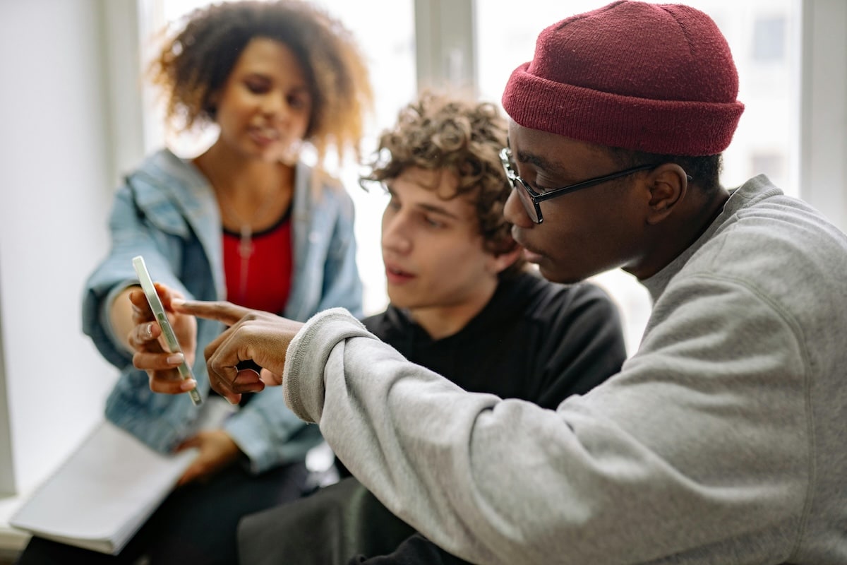 Three students collaborating while looking at a smartphone.