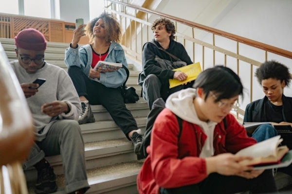 Diverse group of students sitting on stairs reading and using smartphones