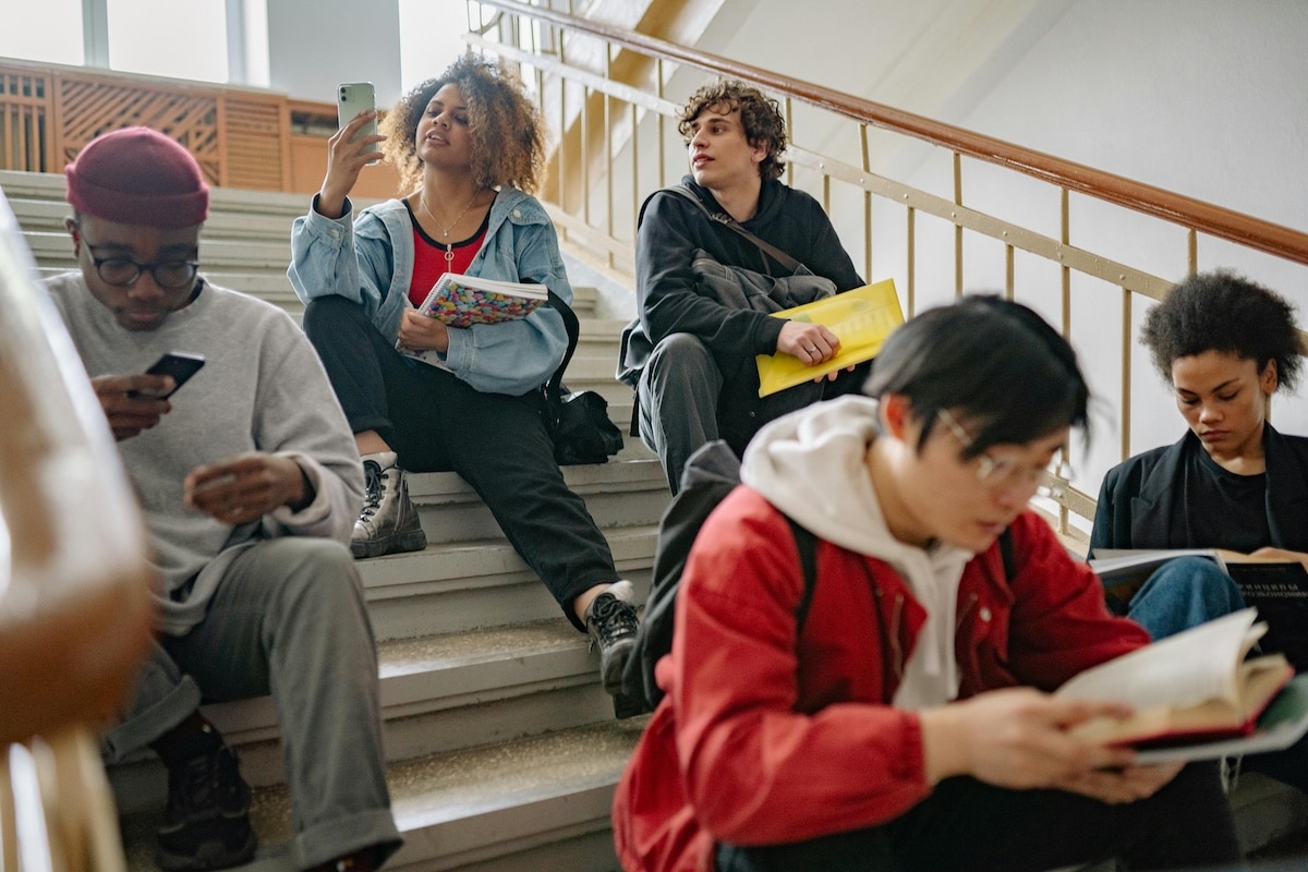 Students Studying and Socializing on Campus Staircase Diverse group of students sitting on stairs reading and using smartphones