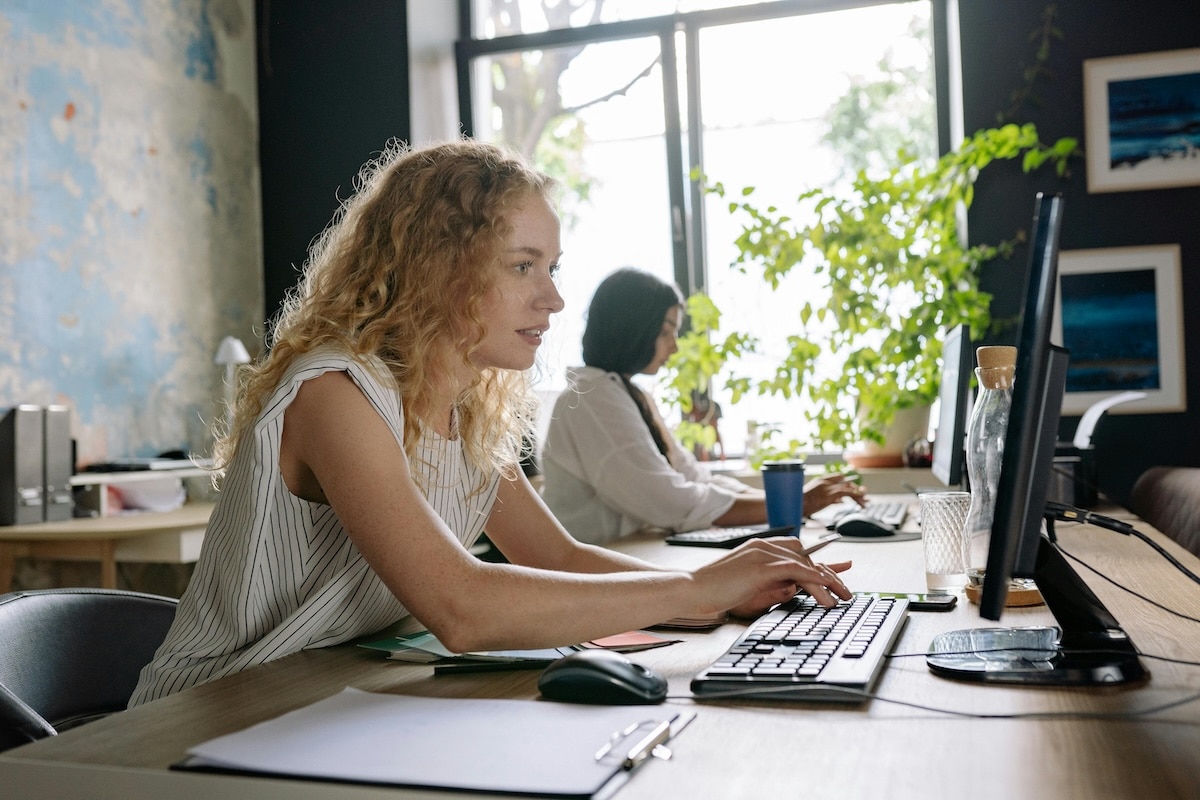 Two women working at desktop computers in a bright modern office