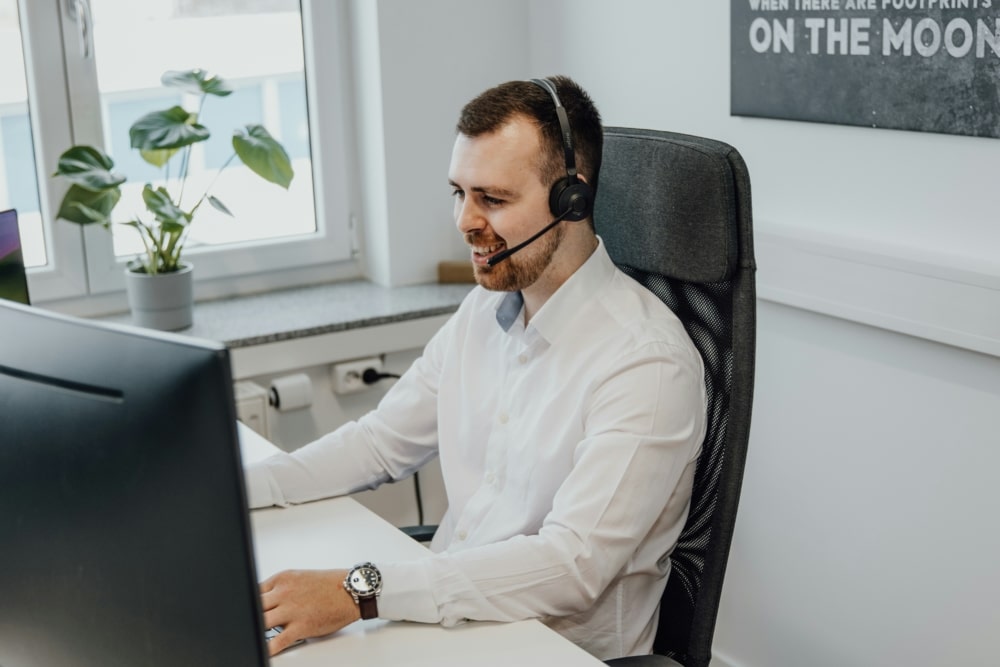 Smiling customer service representative wearing a headset working at a desk in a modern office