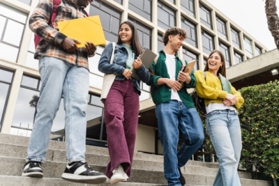 Group of college students walking down steps outside a campus building, smiling and talking.