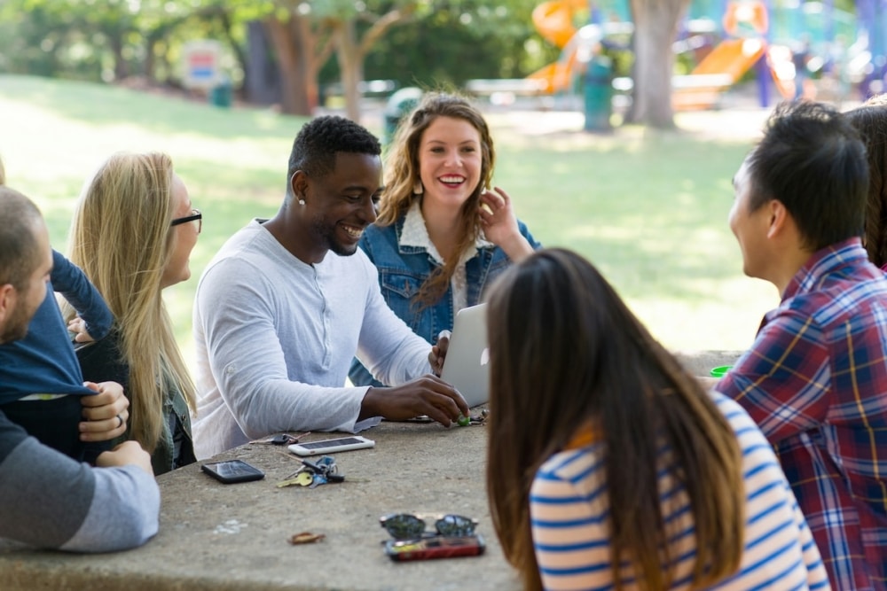 Diverse group of friends laughing and chatting around a picnic table in a park